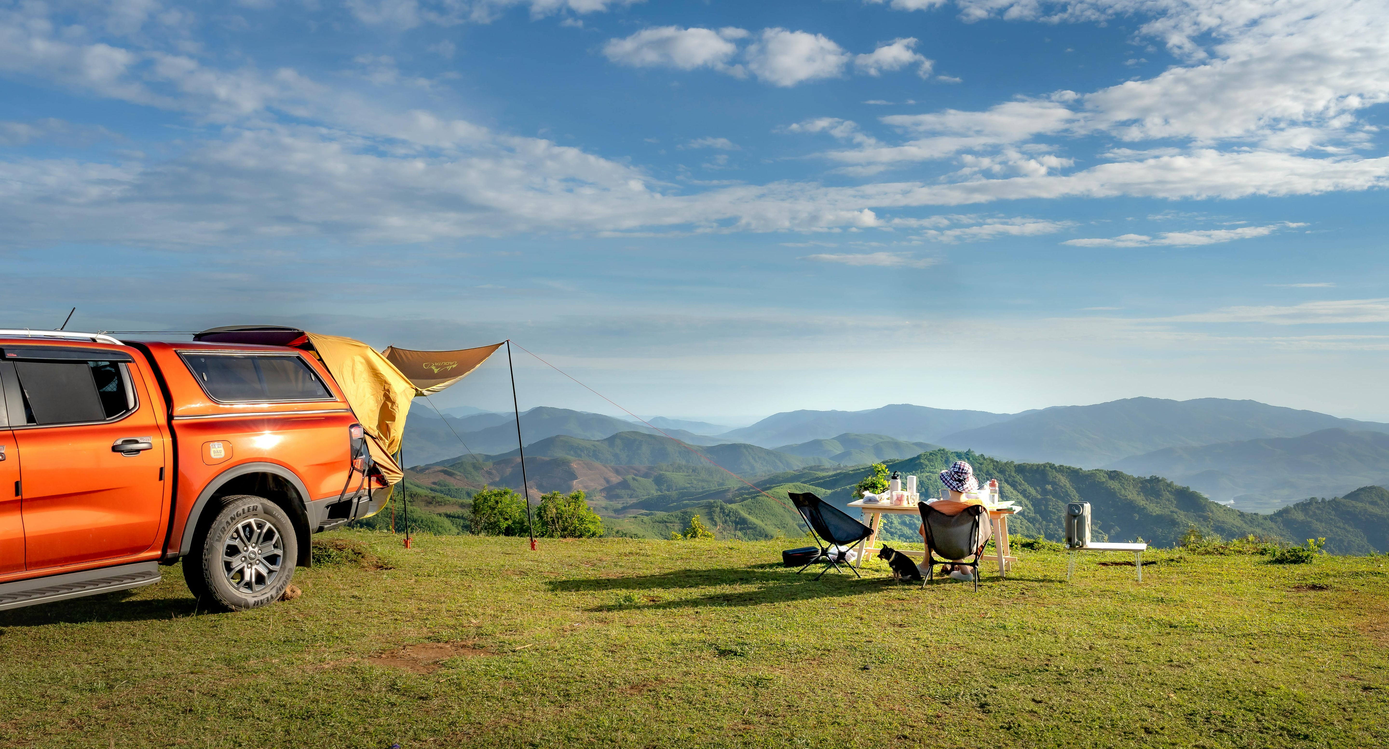 Orange truck with a camper shell parked on a grassy field with mountains in the background